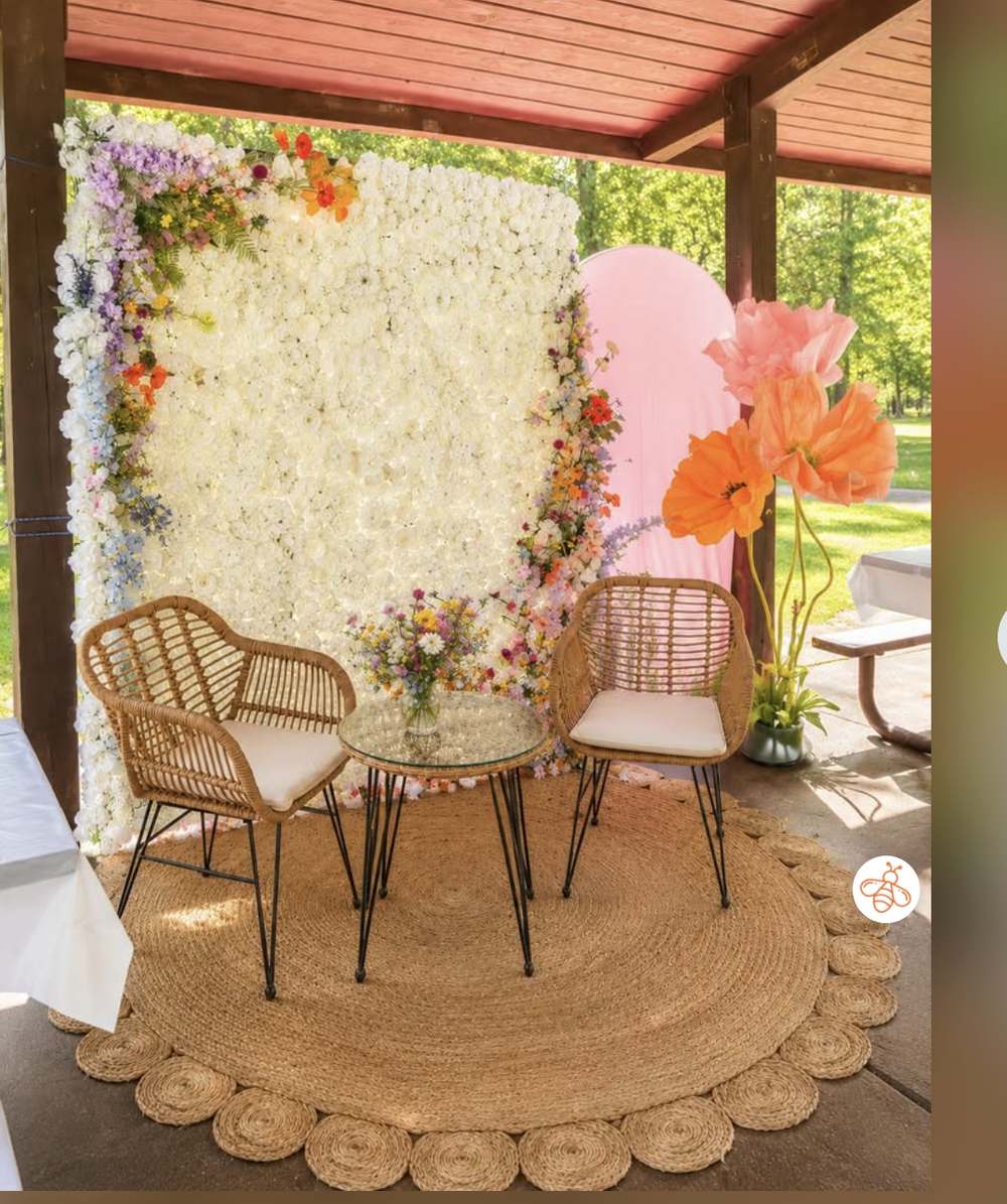 A flower wall backdrop with rattan bistro chairs, styled for a garden party